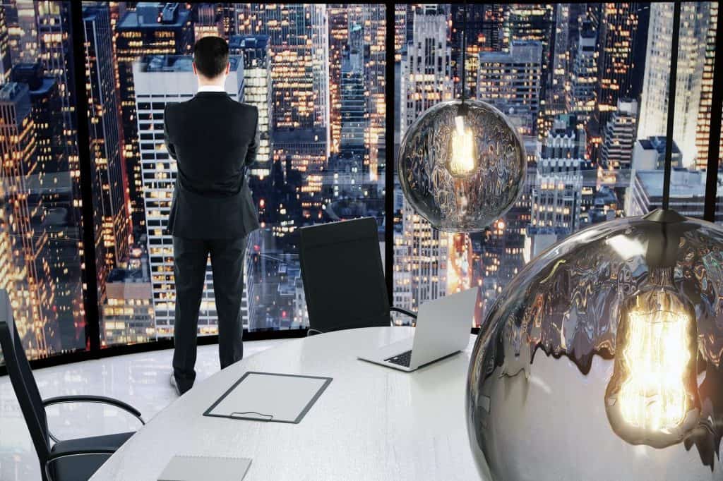 Businessman overlooking city skyline from office window, modern workspace with cityscape background.
