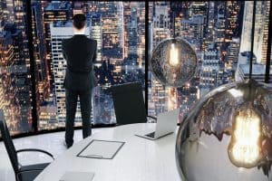 Businessman overlooking city skyline from office window, modern workspace with cityscape background.