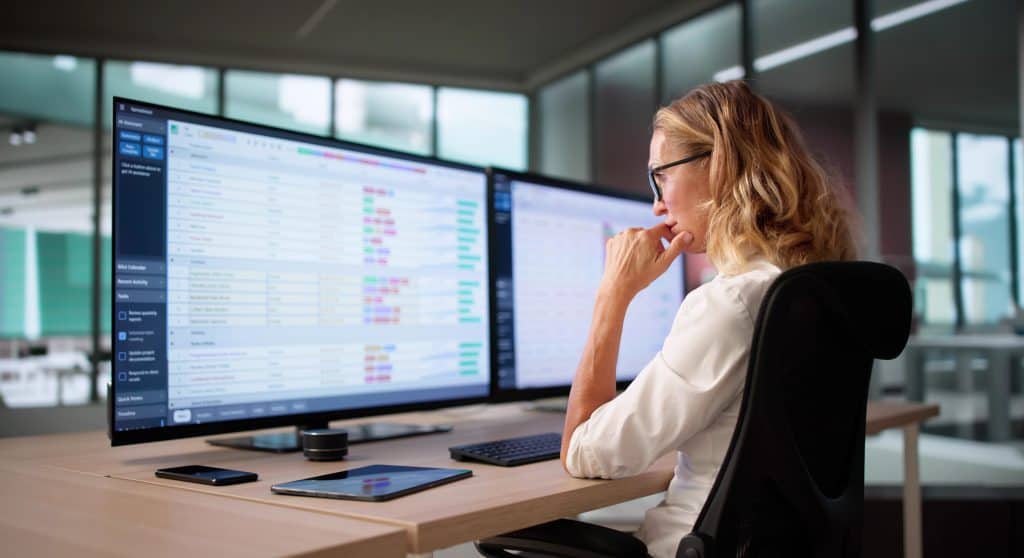 Businesswoman analyzing data on dual monitors in modern office.
