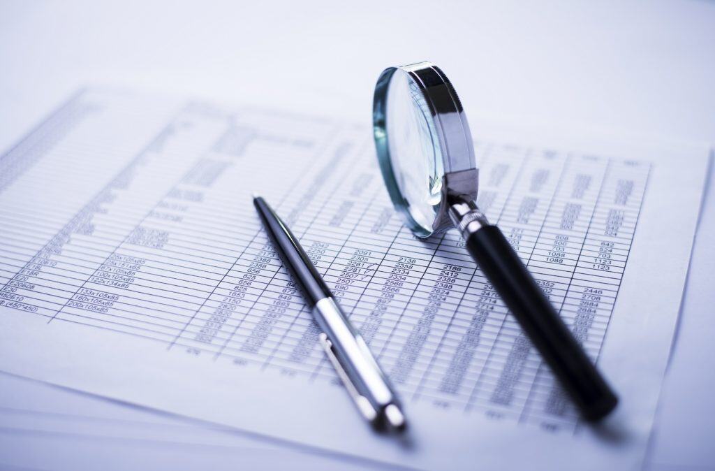 Financial analysis with magnifying glass and pen on documents.