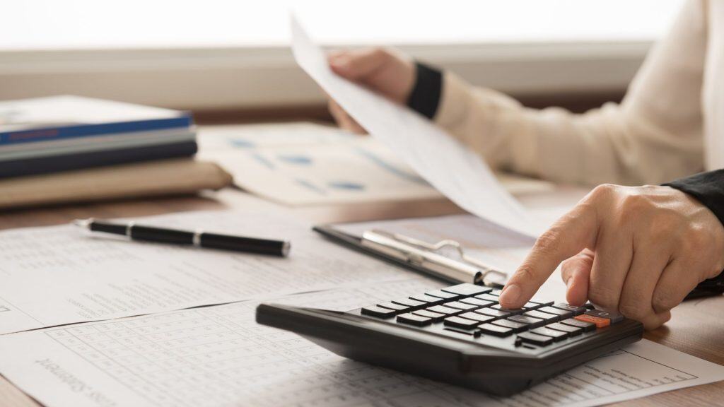 Forensic accountant analyzing financial documents with calculator and reports.