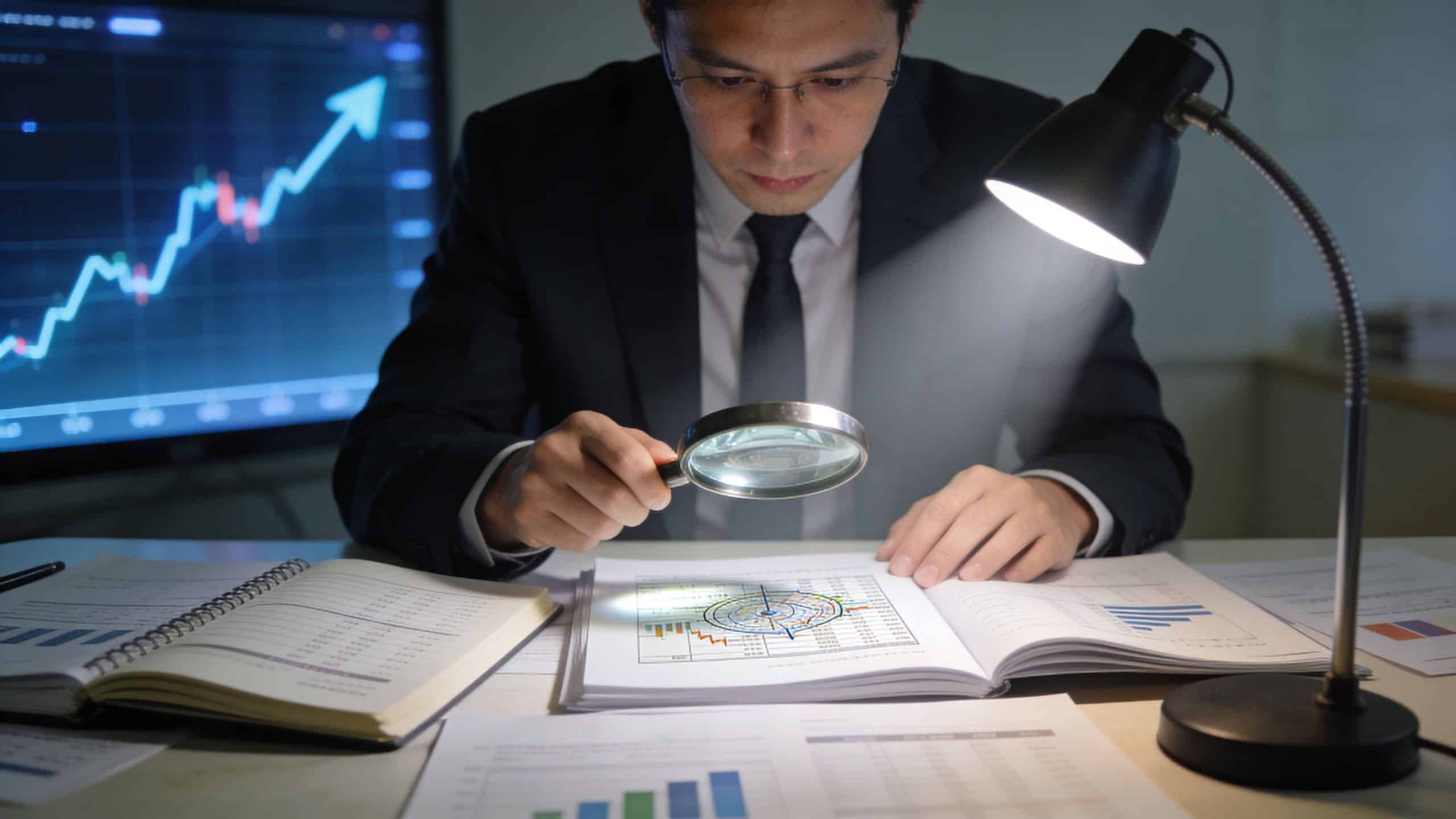 A focused financial analyst using a magnifying glass to carefully examine a detailed business report and charts.