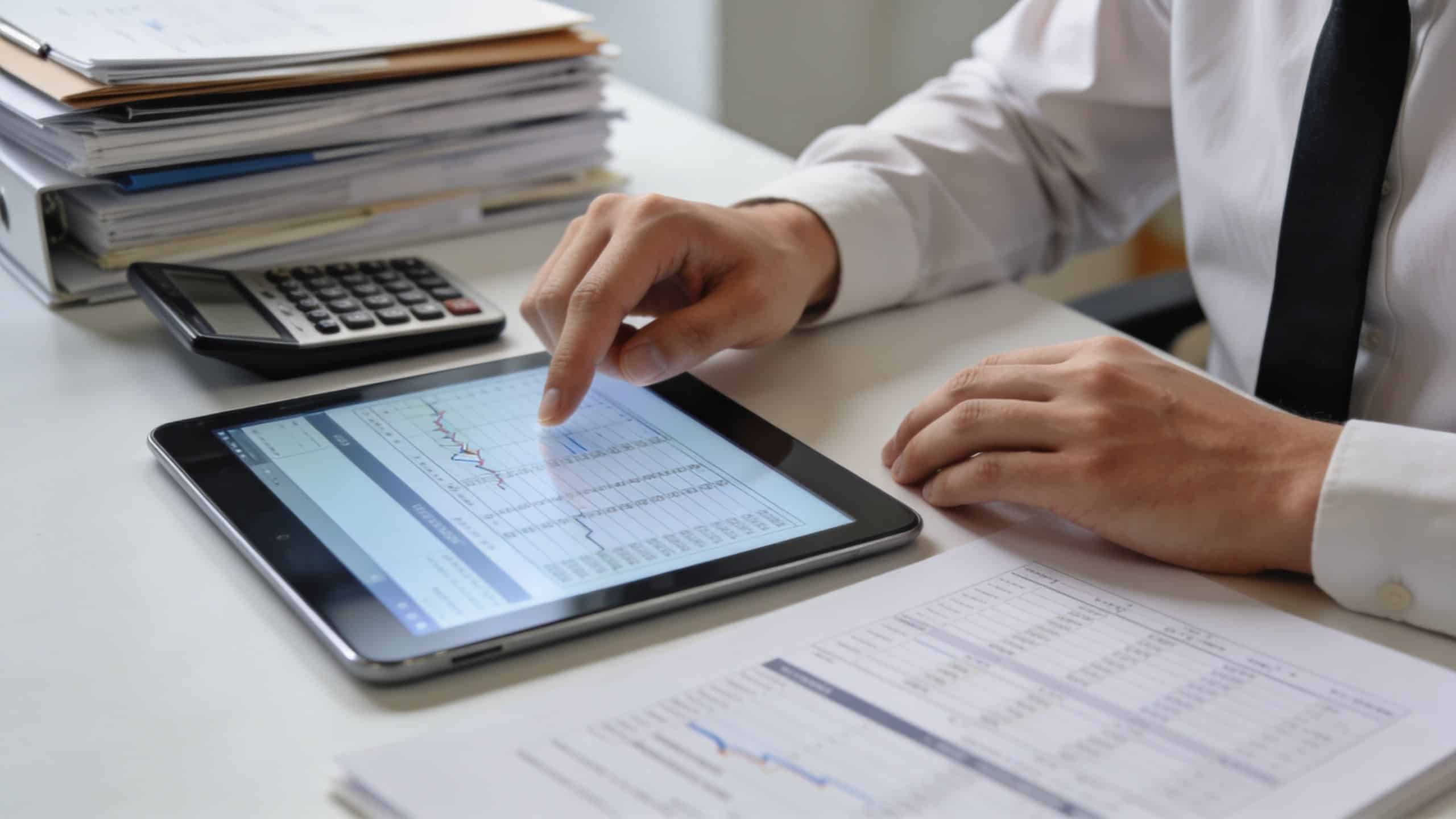 A professional analyzing financial data and business charts on a digital tablet while working at their desk.