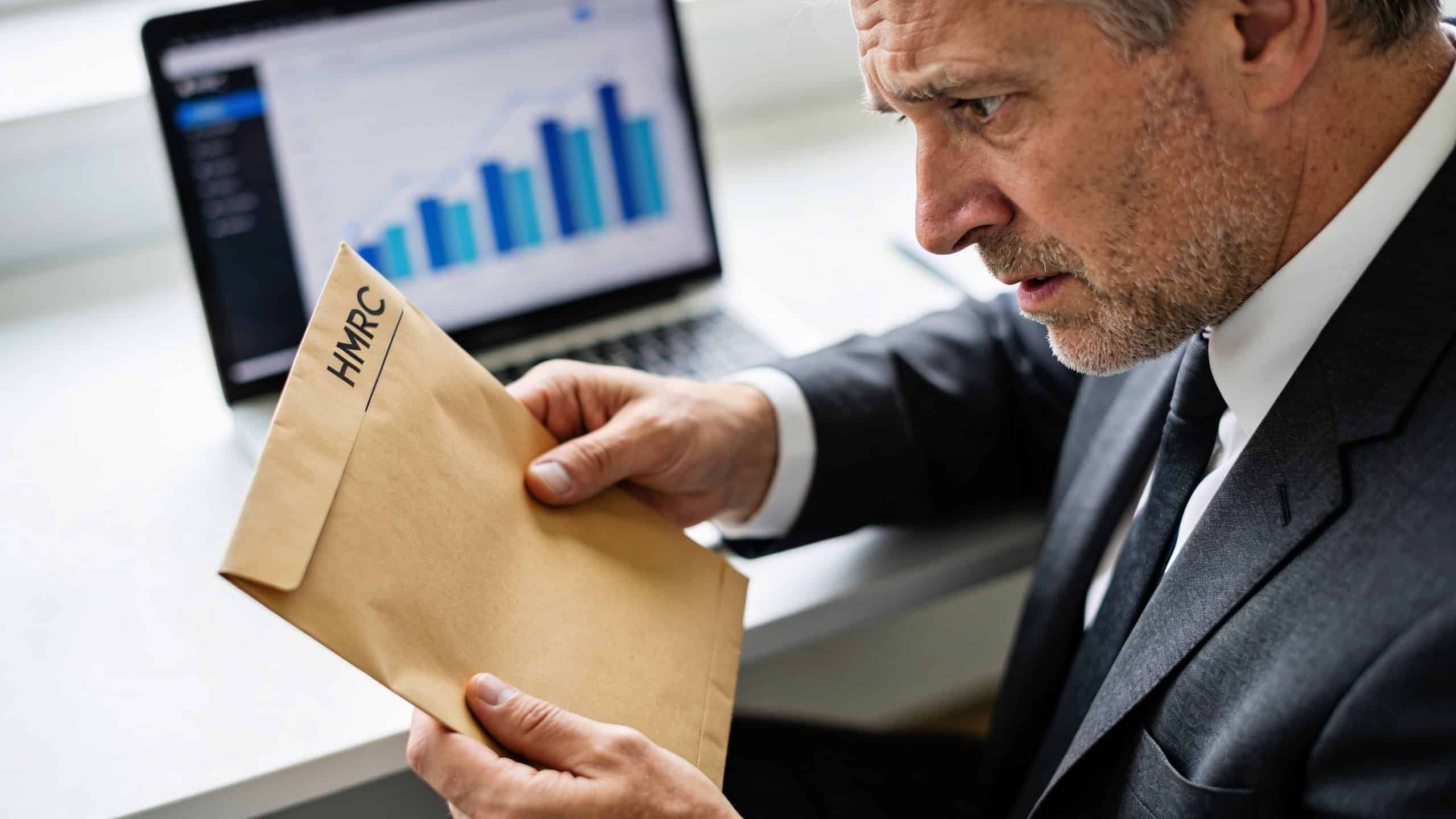 A concerned businessman looking at an official brown HMRC envelope while sitting at his desk