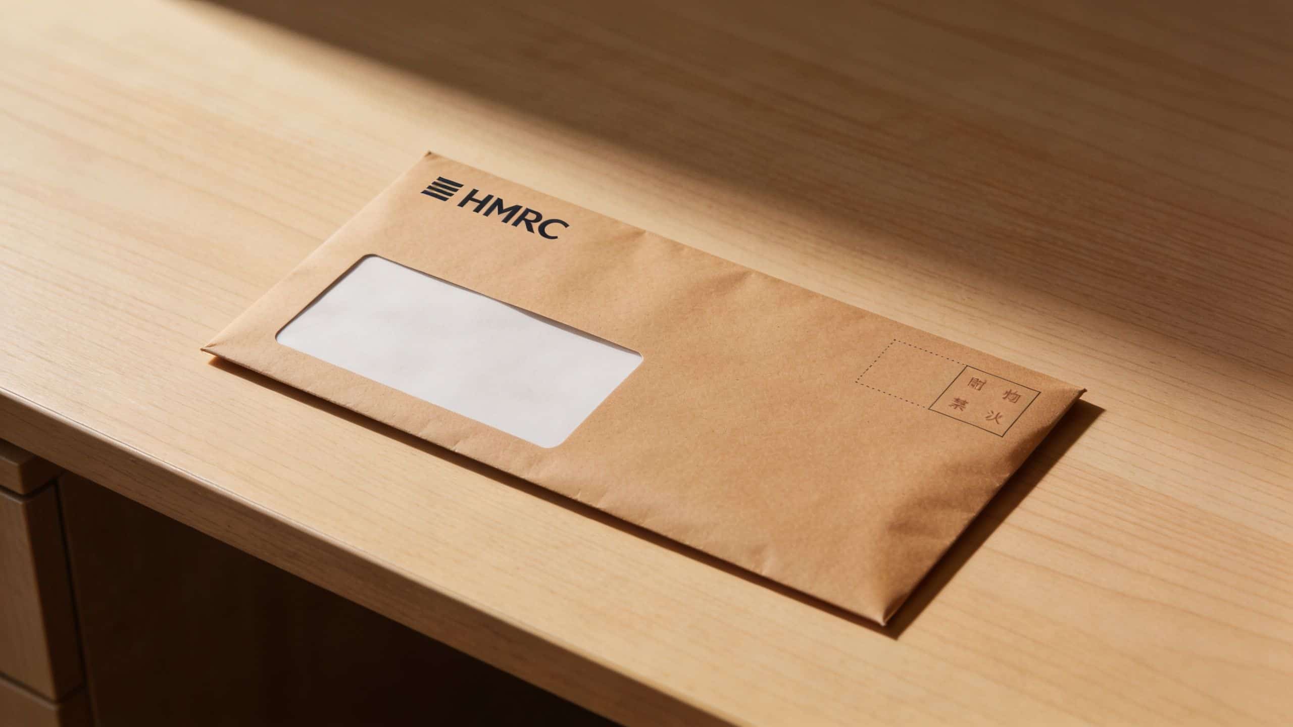 A brown paper envelope with the HMRC logo placed on a wooden desk surface.